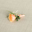 In gentle, diffused daylight this peach rose boutonniere reads as understated refinement-a small arrangement that speaks of careful craft and seasonal softness. The central rose blazes with layered petals, the innermost cupped in a richer golden-apricot tone while the outermost edges soften to a tender peach, creating a natural ombré that seems to glow from within. Tiny gypsophila blooms punctuate the composition like shy stars, their white points adding a light, airy counterpoint to the rose's plushness. Polished green leaves curl into a supportive loop behind the bloom, their glossy faces providing structural clarity and a cool contrast to the warm petals. A filigree of fern and slender foliage threads through the piece, adding a subtle, herbaceous scent that evokes morning walks near Waterlow Park and the hedgerows of Highgate. The stem is meticulously bound in matching peach satin-with even turns and a dainty tuck-so the boutonniere sits flat and secure when affixed to a lapel; Flowers Highgate prepares it with the kind of attention a bride or best man appreciates before stepping out along Highgate High Street. This boutonniere is tender and timeless in equal measure, designed for spring or summer ceremonies, quietly enhancing photographs and close embraces. If you were to ask a local florist to describe it aloud, they might linger on the rose's velvet warmth, the airy whisper of the baby's breath, and the cool, satiny ribbon-sensory details that make this small floral emblem feel both intimate and enduring.