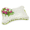 A tender, pillow-shaped memorial composed entirely of small, snow-white chrysanthemums forms the principal surface of this funeral tribute. From a short distance the dense carpet of blooms reads like a soft textile-plush, pillowy and quiet-its tiny petals catching a cool, clear light that suggests a gentle morning at Highgate Pond. At the upper left corner a compact spray of deep fuchsia roses creates the visual and emotional focal point: their velvety petals unfurl with a dignified fullness that speaks of love and remembrance. Nestled among those roses are clusters of fragrant white freesias and petite white buds that add a delicate perfume and a contrast of scale, their bell-shaped faces bright against the white field. Sprays of glossy green foliage and fine fern fronds weave through the composition, lending a fresh verdant frame and a graceful, slightly trailing movement that softens the rectangle's edges. Around the base a pleated, pale green satin ribbon peeks out, its faint sheen and neat looping giving a subtle, ceremonial finish that echoes the natural tones of nearby Highgate woods. The arrangement rests against a clean white background with a soft shadow beneath, accentuating its three-dimensional form and the care of hand-stitching and pinning that holds each stem in place. This classic sympathy pillow is crafted to offer calm and consolation at a funeral or graveside service-an emblem of peaceful rest and enduring memory for those gathering in Highgate Village, just a short walk from the cemetery gates.