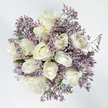 From a top-down perspective, this floral design appears as a tranquil, circular bouquet resting on a pure white background, its simplicity drawing the eye into every gentle detail. At the center, you see around a dozen white roses gathered tightly together. Their petals are thick, smooth, and softly luminous, forming elegant spirals that vary in openness. Some blooms are still composed and bud-like, while others open more fully, revealing layered hearts shaded in subtle tones of ivory and pale, buttery cream. These delicate variations in color give the arrangement warmth and depth, without disturbing its overall purity. Surrounding and weaving between the roses are light, cloud-like clusters of lavender limonium. The tiny flowers of the statice form fine, textured sprays, their lilac and muted purple hues adding a soft veil of colour against the strong white of the roses and background. A few threads of green stem and discreet foliage emerge here and there, reminding you that this is a living, breathing piece of nature. The lighting is even and clear, evoking the gentle daylight that filters across the streets and gardens of Highgate, from Waterlow Park to the quieter residential lanes. At Flowers Highgate, designs like this are often chosen when families wish to send a message of sympathy that is both understated and deeply heartfelt-perhaps for a service near Highgate Cemetery or as a condolence delivery to a home overlooking the Heath. The image captures the essence of that intention: a calm, respectful bouquet that offers comfort and remembrance when words feel too small.