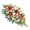 This double-ended coffin spray, shown against a pure white background, presents itself as a balanced, all-round funeral tribute, crafted to sit elegantly along the length of a casket at a Highgate ceremony. The shape is symmetrical and elongated, its central section full and rounded, gradually tapering towards both pointed ends to create a pleasing, leaf-like silhouette. At the heart of the spray, deep red Oriental lilies bloom in wide, star-shaped bursts, their petals rich and velvety with darker markings and prominent stamens that lend the design a sense of depth and intensity. Surrounding these focal flowers, clusters of cream, soft white, and blush pink roses weave gently through the arrangement, some buds still tightly furled, others open to reveal their spiral of petals, offering a tender, timeless expression of love and farewell. Light pink spray carnations, with their frilled, cushiony heads, are scattered evenly throughout, providing texture and a soothing softness. Smaller white chrysanthemums and daisy-style flowers peep between the larger blooms, lifting the palette and adding small flashes of brightness. Fine sprigs of lavender and lilac filler flowers-likely statice or veronica-thread through the piece, introducing cool undertones and a more airy, meadow-like quality, while occasional steel-blue thistle heads stand out with their spiky, sculptural forms and distinctive colouring. All of this is supported by a generous bed of lush green foliage, combining broad, glossy leaves and feathery, fern-like stems that extend out beyond the blossoms to frame the spray in a natural, leafy border. The overall effect is one of calm, dignified beauty, making this arrangement a fitting tribute for funerals and memorials throughout Highgate, where it can offer quiet comfort to gathered family and friends.