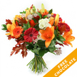 A hand-tied, upright autumn bouquet arranged against a clean white backdrop; the composition reads like a small harvest of the season. Dominating the centre are wide, trumpet-shaped orange lilies with exposed stamens and a few still-closed lily buds that promise more blooms, their smooth petals catching soft studio light. Around them, rich red and bright orange Gerbera daisies offer bold circular heads and dense layered petals, while clusters of creamy white Lisianthus with gently ruffled edges provide a cool, delicate counterpoint. Punctuating the mix are star-like Astrantia blooms with intricate purple-pink centres that add fine, lacey texture. A lush underlayer of deep green foliage - the glossy leaves of ruscus or salal - gives the bouquet a verdant, structured base. Scattered through the arrangement are deeply lobed oak leaves in burnt orange and deep reddish-brown, their crisp autumn tones and jagged silhouettes reinforcing the seasonal mood. The stems are gathered neatly and bound with dark twine or raffia, a traditional hand-tied finish that hints at fresh-from-the-workbench craftsmanship. The arrangement emits a faint green-spicy scent beneath the sweeter lily perfume and feels both generous and composed - suited to a Thanksgiving table, a birthday in October, or a warm welcome home. In the lower right corner of the image a bright orange diagonal banner overlays the photo, plainly stating FREE CHOCOLATE in white letters, calling attention to a seasonal promotion. Available for same-day delivery across Highgate and nearby Hampstead, this bouquet balances rustic texture with polished blooms for a thoughtful autumn gift.