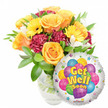 A warm, hopeful Get Well Soon gift ensemble set against a clean white backdrop, lovingly staged to lift the spirits. On the left a generous bouquet blooms in joyful, sunlit tones: soft orange-yellow roses with gently unfurling petals form the visual heart, surrounded by cheerful yellow gerbera daisies whose open faces feel like small suns. Deep burgundy-to-maroon carnations weave textured shadows through the composition, while sprays of delicate white alstroemeria lend a light, airy punctuation that brightens the grouping. Glossy green foliage-broad leaves and slender, verdant stems-frames each bloom and gives the arrangement a freshly gathered, garden-picked impression. The flowers sit in a clear glass vase; you can see stems and water through the transparency, grounding the design in honest, natural materials. To the lower right a round silver Mylar balloon overlaps the bouquet, its mirrored surface catching soft studio highlights. The balloon's center displays a playful cluster of cartoon-style balloons in vivid blue, purple, green, pink and yellow, some patterned with stripes, polka dots and checks, and surrounded by tiny multicolored starbursts along a white border. Bold yellow-and-blue letters proclaim the message Get Well Soon with a friendly shadowed outline; a small KALEIDOSCOPE logo sits discreetly at the balloon's bottom edge. This composition reads as an intimate gesture of comfort and encouragement-a thoughtful hospital or home delivery for a neighbour recovering after illness. As a florist in Highgate I picture this bright duo arriving with a note and a quiet wish for renewed strength, perfect for sending to friends around Highgate Village or by Waterlow Park.