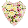 A beautifully dense, heart-shaped sympathy arrangement rests visually against a flawless white backdrop, its carefully chosen flowers and colours combining to express love, sadness, and gratitude. The heart is tightly filled with blossoms so that the overall effect is of a smooth, cushioned surface of petals. At the centre, a small cluster of large cream-to-pale-yellow roses blooms confidently, each rose formed of perfectly spiralled petals that seem to glow softly, symbolising warmth and enduring affection. Radiating outward, numerous pastel pink carnations overlap in every direction, their softly frilled edges building the main body of the heart and creating a plush, comforting texture. In between the pink carnations, white spider chrysanthemums stand out with their many long, thin petals fanning out from bright green centres, adding a crisp, slightly spiky texture that breaks up the softness and brings a touch of brightness to the design. Scattered thoughtfully throughout are deeper magenta-pink lisianthus flowers, their bell-shaped, lightly pleated petals introducing a more intense colour that adds emotional depth to the gentle palette. Tiny hints of fresh green foliage peek between the blooms, giving the piece a natural, garden-like feel while still keeping the focus firmly on the flowers. At the pointed tip of the heart, a soft pink ribbon can be seen just emerging, suggesting that the design is ready to be placed at a funeral, cremation, or memorial service in Highgate, perhaps near Highgate Cemetery or a local chapel. The clean white background keeps all attention on the heart, allowing those who view it-whether in a quiet Highgate home or at a formal service-to see in the flowers a visual expression of remembrance, compassion, and unspoken words.
