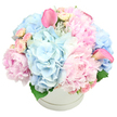 A beautifully styled hatbox arrangement is shown against a crisp white background, its generous mix of pastel flowers creating an impression of softness and quiet celebration. The container is a round, matte white box with a discreet ridge around the top edge, understated but elegant. From it rises a full, domed bouquet dominated by cool light blue hydrangeas, whose clustered florets form broad, cloudlike masses of colour. Intertwined with them are large pink peonies, some blown open to reveal layers of delicate, ruffled petals, others still curved inward, promising more to come. Smaller blush-toned spray roses and tiny rosebuds are carefully woven between the larger blooms, adding fine texture and gentle fluctuations in pink that keep the eye moving. Two bold fuchsia-pink calla lilies extend gracefully above the pastel dome, one on either side of the composition, their smooth, trumpet shapes catching the light and lending a contemporary edge to the otherwise classic mix. A few glimpses of deep green foliage at the base provide just enough contrast to sharpen the colours without disturbing the bouquet's soft mood. The lighting feels like natural daylight, as if the arrangement has just been placed on a bright white table in a Highgate flat near Archway Road, giving the flowers a fresh, just-arrived quality. This design feels ideal for sensitive yet joyful occasions-welcoming a new baby, sending gentle sympathy to a family in Highgate, or decorating a quiet celebration at home. The balance of blue hydrangeas, pink peonies, roses, and sculptural calla lilies speaks of expert local craftsmanship and an eye for both harmony and emotion in floral design.
