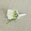 A single white orchid boutonniere rests gently on a softly textured, light beige fabric, the woven surface reminiscent of natural linen often seen in elegant townhouses around Highgate Village. At the heart of the piece is a pristine Phalaenopsis orchid bloom, its broad, velvety petals a pure, luminous white that curls outward in a graceful arc. At the centre of the flower, a delicate hint of pale yellow glows from the throat, adding quiet warmth and depth to the otherwise cool, serene palette. Surrounding the orchid, tiny heads of white baby's breath gather like a cloud, each miniature bloom forming a halo of airy texture that softens the outline of the boutonniere and lends it an almost ethereal quality. Threaded between these dainty flowers are fine, feathery strands of vibrant green foliage, likely a light asparagus or maidenhair-style fern, their slender fronds adding movement and a fresh, garden-picked feel, as if cut that morning from a shaded corner near Waterlow Park. The stems of the orchid, baby's breath, and greenery are neatly aligned and wrapped in a smooth, bright white satin ribbon, the fabric drawn tight and tied into a small, understated bow that sits close to the base, signalling it is ready to be pinned to a lapel. Soft, even lighting falls across the composition, highlighting subtle shadows along the petals and the gentle sheen of the ribbon, while the neutral background allows the crisp whites and clean greens to stand out without distraction. The overall mood is one of quiet sophistication and timeless romance, perfectly suited to a groom or groomsman walking through the leafy streets of Highgate on a wedding morning, or any formal occasion where simple, refined floral details carry deep emotional meaning.
