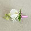 A delicate orchid boutonniere is laid horizontally on a softly textured, light beige linen-style fabric, the neutral background allowing every floral detail to stand out with quiet elegance. At the centre rests a single, flawless white Phalaenopsis orchid, its broad, velvety petals curving open like wings. The heart of the bloom shows a gentle wash of pale yellow with the faintest blush of pink at the throat, giving the flower a luminous, almost porcelain quality. Around the base of the orchid, clusters of fine white baby's breath form a cloud-like halo, each tiny bloom adding airy volume and a sense of romance, reminiscent of mist in nearby Waterlow Park on an early Highgate morning. Slender, vivid green leaves peek out behind the flowers, their smooth surfaces providing a fresh contrast to the softness of the petals. Just to one side, two small lime-green orchid buds remain tightly closed, hinting at new life and the unfolding of a special day. The stems are neatly gathered and wrapped with a slim, bright fuchsia satin ribbon, tied into a petite, perfectly formed bow whose sheen catches the gentle, even lighting. The overall impression is of refined simplicity and thoughtful craftsmanship, a piece easily imagined on a groom's lapel at a Highgate Village wedding, a prom at a local school, or an intimate celebration by Hampstead Heath. The lighting is soft and calm, highlighting subtle textures-the faint weave of the fabric, the satin gloss of the ribbon, and the orchid's silky petals-creating a serene, poised image that speaks of care, freshness, and understated celebration.