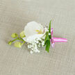 An exquisitely detailed boutonniere is laid out on a natural linen cloth in a soft oatmeal tone, the subtle weave of the fabric giving a gentle, tactile backdrop. At the heart of this buttonhole is a flawless white Phalaenopsis orchid, its wide petals smooth and luminous, opening in a calm, symmetrical curve. The centre of the orchid glows with a delicate yellow-orange hue, brushed with the faintest touch of pink, drawing the eye inward to its intricate throat. Around this focal bloom, clusters of tiny Gypsophila-baby's breath-create a mist of miniature white flowers, their cloud-like texture adding lightness and romance to the overall design. Tucked between these dainty florets are slender, fresh green leaves, offering crisp lines and a vibrant contrast that keeps the composition from feeling too ethereal. Extending from one side, a short stem carries three rounded, pale green orchid buds, tightly closed yet full, hinting at blossoms still waiting to open-much like the anticipatory hush before ceremonies in Highgate's local venues and gardens. The stems of the boutonniere are expertly bound in a bright pink satin ribbon, wrapped smoothly and finished with a petite bow, its glossy loops and short tails adding a charming pop of colour and a modern twist to this classic piece. The overall effect is one of quiet sophistication and personal detail, suitable for weddings, proms, or special gatherings around Highgate, from intimate celebrations near Highgate Woods to smart receptions along Archway Road. Every element feels purposefully placed, as if arranged by a florist who understands both the craft and the emotional weight of life's important moments.