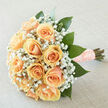 A rounded cluster of peach roses, each petal layered like a cashmere swirl, forms the heart of this bouquet, surrounded by an airy halo of white gypsophila that catches the light like scattered confetti. The composition is anchored by rich, emerald foliage that both contrasts and complements the warm apricot tones, shaping the bouquet into a softly domed silhouette ideal for carrying down a leafy Highgate lane. The stems are gathered and wrapped in a textured blush ribbon, fastened with pearl-topped pins that add a quiet, tactile luxury to the handle-small details we favour when preparing pieces for weddings near Hampstead Heath or for intimate ceremonies on South Grove. Photographed in gentle, diffuse daylight, the arrangement reveals subtle gradations in colour: cream at the petal bases, peach-rush at the outer edges, and the cool shine of fresh leaves. The effect is luminous, as if the blooms hold a faint inner glow. The scent is mild and fresh: the green cleanness of newly cut foliage woven with the soft perfume of roses and the whisper of gyp, a fragrance that comforts rather than overwhelms. As a local florist, I envision this bouquet being chosen for its timeless, tender character-perfect for a bride seeking understatement or for marking an anniversary with sincere warmth. Flowers Highgate prepares and hand-ties each stem with the same considered touch you see here, mindful of local deliveries across Highgate and nearby streets like Archway Road and Hornsey Lane.
