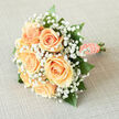 This bridal bouquet, prepared with local care from Flowers Highgate, reads as a tribute to soft romance: six or so lush peach roses clustered closely so their creamy, spiralling petals form a single warm heart. Surrounding them, frothy clouds of white gypsophila create a diaphanous border that softens the silhouette and allows light to glide across the blooms, lending a luminous, almost ethereal quality. Deep emerald leaves and slender glossy sprigs provide a darker counterpoint, anchoring the composition so the peach tones feel richer and more luminous by contrast. The stems are hand-tied and swathed in a peach satin ribbon, neatly finished with a row of delicate pearls that catch the light-a finishing touch that feels both nostalgic and refined. Bring the bouquet close and you notice a subtle fragrance, fresh and floral without being overpowering, like a short walk through a walled garden in Highgate on an early summer morning. This piece suits a bride seeking timeless elegance, a small civil ceremony in Highgate Village, or an intimate reception near Waterlow Park. It's designed to be comfortable to carry, to photograph beautifully in both natural and soft indoor light, and to remain tender as a keepsake. The arrangement's balance of texture, colour and modest ornamentation shows careful florist technique and a sensitivity to classic bridal style, making it an understated emblem of celebration and hope.