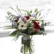 This arrangement is a lyrical interplay of deep red roses, snow-white gerberas, and subtle, dusky lilac lisianthus, harmoniously nestled in a crystal-clear vase. Graceful sprays of eucalyptus arch outward, their round, silvery leaves capturing the shifting daylight much like the famed Highgate foliage along Hampstead Lane. Clusters of tiny ivory filler blooms add layers of texture, their presence as delicate and fine as early morning mist over Highgate Cemetery. The bouquet is cradled by sculptural green leaves, each surface reflecting vitality and echoing the carefully tended gardens of North London. An undercurrent of rose and eucalyptus fragrance weaves through the arrangement, complementing the sense of occasion-be it marking gratitude, celebration, or gentle remembrance for someone special in Highgate. As light plays across the fresh green stems in the water-filled vase, there's a clear impression of local floristry skill and a deep appreciation for the unique atmosphere that characterises our corner of the city.