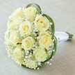 Brought to life by skilled Highgate florists, this close-up, high-angle image reveals a classic, artistically arranged bouquet ideal for weddings or sophisticated events in N6. At its heart, a dense, domed cluster of approximately a dozen pale ivory and soft yellow roses displays tight, unfurling petals, portraying both freshness and refined grace. These luminous blooms are interspersed with abundant baby's breath, whose tiny, snowy blossoms impart a cloud-like softness and gentle radiance, reminiscent of Highgate's tranquil mornings. Deep green foliage curves elegantly around the roses, framing them with modern flair without detracting from the bouquet's serene colour palette. The stems, neatly wrapped in crisp white satin ribbon off to the right, signal a readiness for carrying-perhaps down the aisle at a wedding in Kenwood House or as part of a cherished anniversary celebration. The arrangement rests at a diagonal over a lightly textured linen in soft cream, focusing all attention on the expert craftsmanship and fresh beauty of the flowers themselves. Subtle and sophisticated, this bouquet exudes purity and romance and serves as a timeless symbol of love for couples and families celebrating life's important milestones across Highgate.