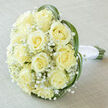 This bridal bouquet reads as a quiet portrait of refinement: a rounded cluster of creamy yellow roses, each bloom opening into a spiralled heart, cushioned by delicate sprays of white baby's breath. The palette is soft ivory and pale butter, a gentle warmth underscored by the feather-like texture of Gypsophila which breathes lightness into the dense rose heads. Thin, vibrant green blades-reminiscent of bear or lily grass-arch around the outside, their elegant curves lifting and containing the flowers while introducing a modern, linear contrast to the classic roundness. The stems are visible at the base, gathered and wrapped in pristine white satin ribbon that feels smooth and reassuring in the hand; the binding is tidy and discreet, the knot steady for carrying down an aisle. The bouquet rests upon a neutral, off-white to light taupe linen surface whose subtle weave gives a whisper of homespun tactility, and the soft, diffused lighting casts gentle shadows that reveal the roses' layered texture without harsh highlights. Scent is implied more than asserted-a faint, clean floral note, the soft sweetness of rose undercut by green freshness. As a local Highgate florist might say, this piece suits a garden-soaked morning near Highgate Pond or a small family gathering in the village-perfect for brides seeking understated beauty, for anniversary gifts, or for moments when sincerity and simplicity are paramount.