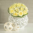 Creamy yellow roses form the heart of this arrangement, each bloom gathered tightly so their ruffled centers open like small, private gardens. A delicate halo of baby's breath-feathery white gypsophila-surrounds the roses, its tiny stars softening the silhouette and introducing an almost cloudlike lightness. The container is a white wicker orb, contemporary yet warm, its airy architecture giving the bouquet room to breathe and casting subtle shadows that emphasise the roses' gentle curves. Nearby woven spheres, minimalist and tactile, provide a playful counterpoint: modern accents that reinforce the composition's sculptural quality without disturbing its quiet refinement. Wisps of curling greenery thread through the arrangement, adding rhythm and a slim contrast of fresh green that frames each rose with an understated flourish.The scent is evocative-a clean, sun-washed perfume of roses mingled with the green, earthen note of freshly cut stems-soothing and bright, like a morning stroll around Highgate Village. In the hands of an experienced florist, this piece becomes a thoughtful expression for a wedding table, a calm centrepiece at a celebratory luncheon, or a tender gift to mark a new chapter. Delivered carefully across Highgate and into neighbouring Hampstead and Archway, it communicates gentle optimism and refined simplicity, perfect for anyone who appreciates craftsmanship, seasonal freshness, and quietly modern design.
