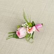Delicately composed by the skilled hands of Highgate florists, this boutonniere exudes understated luxury against a softly woven beige background evocative of elegant interiors in North London townhouses. The centerpiece, a soft pink rose with petals tightly wrapped in a graceful spiral, anchors the arrangement in romance, its colour gently lightening outward from a rich core. Flanking the rose, a petite ruffled bloom in blush or peach reveals intricate yellow shading and dark flecks, lending complexity and subtle drama. White baby's breath blossoms float gently through the design, matched by green, ball-shaped mini mums that introduce refreshing contrast. The foliage-sleek, verdant, and abundant-ranges from wispy blades to deep green, folded leaves that form a naturalistic, modern base. The bundled stems are encased in a wide, deep green leaf and fastened with a lustrous fuchsia pink satin ribbon, tied in a neat, celebratory bow. This piece, reminiscent of weddings, proms, and milestone gatherings from Waterlow Park to Swain's Lane, is more than an accessory: it's a keepsake crafted with love, artistry, and a signature Highgate flourish.