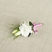 A delicately crafted wedding boutonnière rests on a softly textured, light beige fabric that looks like finely woven linen, its gentle oatmeal tones evoking a quiet Highgate morning. At the heart of the arrangement is a single white lisianthus bloom, fully open and perfectly formed, its ruffled petals layered like fine silk, glowing softly against the neutral background. Two slender lisianthus buds, still closed and tinged with creamy pale green, nestle just beside the main flower, suggesting the promise of moments still to come. Around them, clusters of tiny white gypsophila float like a cloud, each miniature bloom adding lightness and air, reminiscent of blossom drifting over nearby Waterlow Park in spring. Dark green leaves provide depth and structure, one broader leaf cradling the flowers while slim, grass-like strands sweep diagonally to the left, introducing movement and a fresh, garden-picked feel. The stems are neatly bound at the base with a soft pink satin ribbon, tied into a small, tidy bow whose gentle sheen catches the light and adds a whisper of romance. The overall design feels intimate and considered, ideal for pinning to a groom's lapel at a Highgate Village ceremony or for a prom corsage on a summer evening. The lighting is even and flattering, revealing every curve of petal and subtle shift of green, capturing the calm, hopeful mood of a special day about to begin.