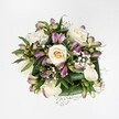 Overhead view of an elegant hand-tied bouquet laid against a pure white background, showing creamy white and soft ivory roses surrounded by lilac and mauve alstroemeria, baby's breath, and deep green foliage, as if freshly prepared in a Highgate flower studio. Each rose sits at a different stage of opening: some are tight buds with a faint pale-yellow heart, while others are fully unfurled, their spiralling petals forming plush, rounded cups that look velvety and cool, almost touchable. Threaded between these focal blooms, alstroemeria stems arc out gently, a mix of slim, closed buds and half-open flowers whose slender petals fade from soft lavender to purplish-pink, accented with fine green streaks that echo the foliage. Tiny gypsophila blossoms, like pinpricks of white foam, cluster in airy clouds, softening the transitions between the larger flowers and adding a dreamy, romantic haze. The base of the arrangement is formed by broad, glossy green leaves that curve and fold around the flowers, giving the composition structure and a sense of fullness without heaviness. The clean, bright lighting suggests natural daylight, as if the bouquet were photographed near a Highgate Village window overlooking tree-lined streets, capturing every subtle texture and colour nuance. This balanced, medium-sized bouquet feels ideal for quiet celebrations, thoughtful thank-yous, or gentle sympathy, its calm palette and harmonious shapes evoking tenderness and reassurance. Though there is no visible wrapping or vase, the composition reads as professionally designed, the kind of refined arrangement a local Highgate florist might send out for same-day delivery to homes near Waterlow Park or along Swain's Lane, carrying with it a whisper of comfort and understated grace.