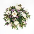 Overhead view of a hand-tied, circular bouquet laid on a crisp white background, its colours glowing as clearly as a spring morning over Highgate Wood. At the heart of the arrangement, several creamy white roses unfurl in soft spirals, their petals shifting gently from warm ivory to pale champagne, some fully open and plush, others still modestly cupped. Threaded between them are deep purple and lavender Alstroemeria buds, their slender petals tightly furled, brushed with magenta and fading to fresh green at the base, adding a sense of movement and anticipation. Tiny clouds of white gypsophila hover throughout, each cluster of baby's breath forming a fine, lacy mist that softens the composition and gives it a weightless, celebratory feel. Surrounding and supporting the blooms, broad, glossy dark green leaves form a nest of foliage, their smooth surfaces catching the soft, even light so that subtle highlights run along each vein. There is no visible vase or ribbon in the frame, only the bouquet itself, perfectly centered, every detail clearly outlined against the pure white space. The lighting is gentle and shadowless, as if the bouquet had been placed near a large window in a Highgate village townhouse just before delivery. The mood it creates is calm and refined, ideal for a thoughtful anniversary surprise, a quiet wedding celebration at a local Highgate venue, or a message of comfort sent across the neighbourhood. The interplay of classic white roses with contemporary purple Alstroemeria buds captures an elegant balance between tradition and modern style, conveying hope, tenderness, and a poised sense of joy.