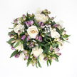 Against a brilliant white background, this top-down view captures a tranquil bouquet that feels perfectly at home in Highgate's calm, leafy streets. At the centre, creamy white roses unfold in stages: some fully open, their velvety petals curling back to reveal soft ivory depths with a touch of peach warmth, others still slightly closed, forming rounded cups that hold their beauty in a more private way. Threading through these central blooms are elegant purple alstroemeria buds, slender and gently arched. Their pointed tips carry rich shades of lavender and deep purple, gradually fading into soft green and subtle pinkish tones towards their bases. Many of the Peruvian lily buds remain tightly wrapped, indicating blooms yet to come, while a few are just beginning to separate, hinting at the fine striations inside. Light, feathery sprays of white baby's breath are scattered among the roses and lilies, each tiny blossom adding a mist-like softness that makes the bouquet feel as though it is wrapped in a gentle haze. Surrounding this inner cluster, deep green foliage fans out in broad, glossy leaves, providing structure, depth, and a natural contrast that highlights the paler flowers. The arrangement is compact and gently spherical, every stem carefully positioned so the bouquet looks complete from every angle. It is easy to picture this design resting on a side table in a Highgate home or brought as a quiet tribute to a memorial gathering near Highgate Wood. The interplay of white, purple, and green creates an atmosphere of peace, thoughtful support, and softly spoken condolence.