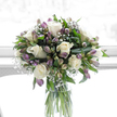 A refined sympathy bouquet stands in a clear glass cylinder vase, its gentle colours and balanced form illuminated by soft, natural light like that falling across a sitting room in Highgate. At the centre, large creamy white roses unfold in smooth, velvety layers, each blossom perfectly cupped and serene, creating a sense of peace and quiet grace. Between the roses, alstroemeria blossoms offer gentle hints of mauve, lilac, and pale green along their slender petals, adding a delicate veil of colour and fine-lined texture. Scattered throughout, airy tufts of white baby's breath create tiny constellations of bloom, filling the arrangement with gossamer lightness and bridging the spaces between the more substantial flowers. Encircling all of this, rich green foliage spreads in varied tones and shapes-broad, glossy leaves near the base and more slender, arching stems toward the edges-framing the bouquet in a way that calls to mind the layered greenery of nearby Highgate gardens and the edges of Hampstead Heath. The vase itself, simple and cylindrical, reveals the straight, cut stems gathered together in clear water, reinforcing the natural, unembellished beauty of the design. Against a bright, softly diffused white background, every petal and leaf stands out with clarity, allowing the bouquet's calm palette and careful structure to speak of compassion. Perfect for condolences or memorial tributes in and around Highgate, this arrangement offers a gentle visual comfort, expressing sympathy and remembrance with quiet dignity.
