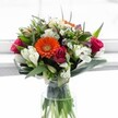 Evoking the gentle light streaming through Highgate's Victorian windows, this lively bouquet bursts with the warmth of an early spring morning. The eye is first captured by a glorious orange Gerbera daisy, glowing from the centre like an unexpected sun, surrounded by a stunning collection of vibrant deep-pink and red roses-some full and fragrant, others tightly coiled in anticipation. White alstroemeria blossoms, with their intricate speckling, wind through the arrangement alongside delicate, daisy-like white chrysanthemums that recall the fleeting bloom of wildflowers on Hampstead Lane. Towards the top, creamy yellow roses add an understated richness, while small touches of soft purple and lavender provide poetic depth and balance. Rich green foliage, both broad and slender, is expertly arranged, embracing the bouquet and offering texture and movement, much as Highgate Woods envelops the neighbourhood in verdant calm. Presented in a minimal clear glass vase with the stems visible below, resting in pure water, the overall effect is one of grace, freshness, and thoughtful design. Perfect as a heartfelt gift, a centrepiece for a Highgate dinner table, or a way to infuse a home near Park Road with cheer, this bouquet celebrates both tradition and the vibrant community spirit found at the heart of Flowers Highgate.