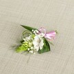 A delicate, handcrafted boutonniere or small corsage rests gently on a softly textured, light beige fabric that looks like natural linen, its neutral tone echoing the calm elegance of a Highgate townhouse interior. At the heart of the arrangement sits a single white alstroemeria bloom, its broad petals opening wide to reveal fine reddish-brown speckles deep in the throat and slender stamens dusted with pollen. Just to the side, a conical spike of vivid lime-green buds, resembling Ornithogalum or ginger-like florets, introduces a striking sculptural shape and a sense of fresh, growing energy. Wisps and clusters of white baby's breath weave through the design like tiny clouds, lending a dreamy, airy softness around the central flower. Supporting everything is a base of deep green, sword-shaped leaves and finer grass-like blades that arc lightly outwards, adding movement and a touch of wild, garden-inspired charm. A glossy pastel pink satin ribbon is tied into a neat, compact bow, positioned toward the right of the stems, its sheen catching the even, gentle light and bringing a joyful note of colour that hints at romance and celebration. The photograph is lit in a way that feels like soft afternoon light drifting in from a Highgate Village window, highlighting each vein in the foliage and each tiny baby's breath blossom. The whole piece suggests a wedding morning boutonniere for a lapel or a dainty corsage for the wrist, a refined floral accent that would feel at home at a ceremony near Waterlow Park or a reception overlooking the leafy streets around Highgate Hill, its fresh scent and quiet beauty capturing the anticipation of a special day.