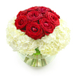This photograph captures an elegant, romantic bouquet designed in a compact, rounded style, set against a bright white background that makes every colour appear vivid and true. At the very top of the arrangement sits a smooth dome of deep red roses, around nine or ten in total, nestled closely together so that their velvety heads form a unified crown of rich crimson. Their petals curl and spiral in layered whorls, some blooms fully open and expressive, others still slightly cupped as if they are slowly unfurling over the course of an anniversary evening in Highgate. Surrounding and supporting this cluster of roses is a full, spherical base of creamy white hydrangeas. The hydrangea blossoms are composed of numerous small florets packed tightly side by side, creating a soft, billowing texture that resembles a cloud of petals. The contrast between the bold, passionate red and the serene white feels both dramatic and gentle, suggesting a balance between intensity and tenderness. All of the flowers are arranged in a clear, round glass vase that resembles a small fishbowl, its curved sides partially filled with water. Through the glass, the clean-cut green stems are visible, fanning out slightly and crossing at natural angles, adding a sense of structure underneath the plush blooms. Reflections on the surface of the vase and the water create subtle highlights that contribute to the overall sense of freshness and polish. With no foliage or extra embellishments, the focus remains entirely on the interplay of colour, texture, and form. This bouquet would sit beautifully on a dining table near Highgate Woods, on a windowsill overlooking the village, or delivered as a thoughtful anniversary surprise, quietly expressing deep affection and enduring commitment.