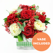 This photograph captures a romantic, celebratory bouquet of red and white roses, perfectly arranged and set before a bright white backdrop, echoing the calm light of a Highgate morning. In the centre of the scene, lush deep red roses mingle intimately with soft, creamy white roses, the petals unfolding in layered spirals that appear almost touchable. The contrast between the passionate crimson tones and the gentle ivory shades creates a harmonious, elegant mood, ideal for gracing a windowsill overlooking the trees of Highgate or a dining table on a quiet lane near Waterlow Park. Threaded throughout the roses are airy clusters of tiny bright red filler flowers, similar to dyed baby's breath; they create a fine, lace-like texture that weaves through the arrangement and softens the spaces between each bloom. Bright, smooth red hypericum berries are tucked among the petals, their rounded forms catching the light and adding a playful, festive sparkle. Surrounding the central mass of flowers, greenery extends outward: dark green leaves lend structure and depth, while slender stems of eucalyptus, with their muted, grey-green leaves, introduce a contemporary, slightly wild note, as if the bouquet incorporates a hint of the nearby Highgate Wood. At the base, the flowers are gathered into a clear rectangular glass vase. Through the vase's transparent sides, straight green stems can be seen standing in clear water, reinforcing the sense of freshness and professional care from a local Highgate florist. A green and white gingham ribbon wraps horizontally around the centre of the vase, its checked pattern adding a touch of rustic charm and homely warmth. In the lower right corner of the image, a prominent orange circular badge carries the white, uppercase message VASE INCLUDED, indicating that the bouquet arrives complete, ready to place as a thoughtful gift for birthdays, anniversaries, or intimate romantic gestures in Highgate.