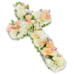 A dignified floral cross arrangement, intended as a funeral or memorial tribute, is captured against a flawless white background, where its soft colours and rich textures feel especially poignant. The cross is constructed entirely from flowers, with no visible framework, forming a thick, lush silhouette that appears almost like a soft pillow of petals. The main flowers are roses in a carefully balanced mix of white, ivory, pale peach, and blush pink, arranged so that the lighter tones form a calm base while the warmer shades offer gentle points of focus along the vertical and horizontal arms. Some roses are wide open, displaying intricate layers of petals, while others remain in half-bud, lending a sense of delicacy and unfolding remembrance. Nestled among them are rounded clusters of white hydrangeas or similar mass florets, adding volume and a billowy, cloud-like effect that softens the entire design. Subtle sprigs of lavender-tinted filler flowers are positioned here and there, providing tiny specks of purple that break up the whites and creams in a refined way. The edges of the cross are traced by discreet glimpses of green foliage, which help define the shape and add a fresh, natural contrast without intruding on the pastel harmony. The lighting is bright and balanced, ensuring that each bloom appears crisp and freshly arranged, as you might expect from a skilled florist preparing tributes for services around Highgate Village, Archway Road, or the peaceful surroundings of Waterlow Park. Overall, the floral cross evokes a sense of peace, hope, and tender farewell, a fitting centrepiece for a church or crematorium service honouring a cherished life.
