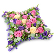 A tranquil floral cushion tribute fills the image, its shape that of a rectangular pillow with gently softened corners, as though inviting the eye to rest upon it. Set against a clean white background, the arrangement's colours stand out clearly without harshness. The florist has densely packed the surface with roses and complementary blooms so that the cushion looks full and plush, like a bed of petals. Large roses in vibrant fuchsia, soft rose-pink, and creamy pale yellow are distributed evenly, their layered petals opening in spirals that catch the light and draw attention to their natural beauty. Between them, rich royal-purple lisianthus flowers add velvety shadows and a sense of calm depth, akin to the quieter corners of Highgate's residential streets on a misty morning. Smaller spray roses in gentle blush tones and airy clusters of lavender and lilac filler flowers, reminiscent of statice or limonium, fill tiny spaces and create an intricate, lace-like effect. The edge of the cushion and many inner gaps are softened with foliage: rounded, silvery eucalyptus leaves introduce a cool, soothing green, while darker, finer leaves add structure and texture without overpowering the flowers. The overall palette of pink, cream, yellow, and purple conveys tender affection and respect, perfectly in keeping with tributes chosen for funerals, cremations, or remembrance services in Highgate and the surrounding area. This floral pillow feels like a symbolic headrest offered to someone dearly missed, expressing sympathy and the wish for peaceful rest. It appears thoughtfully constructed from fresh, carefully selected stems, the kind of arrangement that would be prepared with quiet dedication by Flowers Highgate for local families during their most difficult moments.