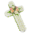 A floral cross designed for a funeral or memorial service is shown against a bright, seamless white background, with a slight shadow adding depth to its form. The cross itself is entirely carpeted in small white chrysanthemums, each button-like bloom positioned close to the next to form an even, padded surface with no visible gaps. The compact clusters of petals lend the piece a velvety texture and a sense of purity, making the cross appear both solid and gently comforting. Following the perimeter of the cross is a fine lime-green ribbon, folded tidily around the frame. It emerges in slim bands beneath the soft mass of white flowers, defining the outline of the arms and vertical beam while adding a fresh, springlike touch of colour. At the heart of the cross, directly at the intersection of the beams, a small, carefully constructed floral accent serves as the focal point. Fully opened roses in pale pink, delicate peach, and creamy white are grouped together, their rounded forms and layered petals creating a sense of tenderness and warmth. They are framed by feathery fern fronds and tiny stems of lavender-toned filler blossoms, which introduce a veil of soft purple and light greenery. The overall atmosphere is quiet and reverent, reminiscent of a solemn gathering in one of Highgate's historic churches or chapels. The cross is clearly intended as a sympathy tribute, suitable for delivery to services near Highgate Cemetery or local crematoria, expressing faith, respect, and the enduring affection of those saying goodbye.