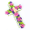 Captured on a bright, seamless white background, this floral cross appears gently angled from the upper left towards the lower right, offering a sense of quiet movement and depth. The outline of the cross is defined by a full collar of white spray chrysanthemums, each small bloom nestled closely together to create a plush, cloud-like border that feels serene and pure, much like the stillness of an early morning walk through Highgate's leafy streets. Peeking just beyond that white edge is a slim band of pale green ribbon or folded foliage, its soft colour adding a polished finish and a hint of natural freshness that echoes the surrounding greenery near Waterlow Park. Within this thoughtful frame, the centre of the cross is richly decorated with an array of colourful flowers. Fully open roses in vivid fuchsia pink and soft, creamy yellow punctuate the design along the vertical and horizontal arms, their layered petals forming elegant focal points. Between these roses, clusters of lime-green button chrysanthemums create rounded islands of texture, their bright hue offering a lively contrast and modern twist. Threaded delicately throughout are smaller blooms in deep purples and violets, likely lisianthus or statice, whose darker tones lend a quiet, reflective quality well suited to a funeral, memorial, or graveside service in the Highgate area. The bright, even lighting makes every detail stand out, from the velvety rose petals to the neat pleats of green ribbon. Crafted with the sensitivity and expertise of local florists such as Flowers Highgate, this floral cross conveys both respect and affection, honouring faith, love, and cherished memories with a beautifully balanced mix of colour and calm.