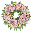 Resting on a pure white background, this carefully crafted funeral wreath forms a complete circle of soft colour and texture, reminiscent of a quiet, reflective moment in one of Highgate's peaceful gardens. The design centres on large, fully opened roses in shades of dusty lavender and antique mauve, their numerous petals layered densely to create plush, rounded blooms. Each rose is positioned with intention, spaced evenly around the wreath to guide the eye along the ring. Between these focal flowers, smaller blush pink spray roses gather in clusters, some still tightly closed and others partially open, contributing a delicate, almost whispered touch of warmth. The combination of the cool lavender tones and the gentle pinks feels both soothing and tender. All of the blooms sit atop a foundation of rich, dark green fern fronds, probably leatherleaf or a similar variety, with finely segmented leaves that splay outward from beneath the flowers. Where the ferns peek through, they lend a fresh, natural contrast, their deep green underscoring the pastel shades above. Tucked into the arrangement are subtle hints of darker filler greens and possibly tiny buds, which create little pockets of shadow and help to define the circular shape. The lighting across the scene is soft and even, allowing the colours to appear true and calm, with no harsh highlights. This wreath embodies a sense of respectful serenity and compassion, making it the kind of arrangement a family might choose for a service in Highgate, to honour a loved one with understated beauty and a lasting symbol of remembrance.