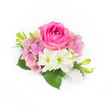 Set against a pristine white backdrop, this compact corsage reads like a whispered promise of spring - a lush bubblegum-fuchsia rose sits slightly off-centre, its velvety petals tightly swirled at the heart before unfurling into a plush, glowing bloom. Around it, a soft halo of pastel pink and lavender hydrangea florets creates gentle volume, each tiny petal catching the light like fragile paper fans. Two creamy, trumpet-shaped blooms-reminiscent of small amaryllis or lilies-nestle beneath the rose, their greenish throats adding a cool, fresh counterpoint to the warm pinks. Broad, deep-green leaves fan out at the base, glossy and substantial, grounding the composition with a garden-fresh weight. Sprays of slender green buds tipped with a hint of yellow push upward, suggesting movement and the quiet promise of more flowers to come, while a small cascade of lustrous white pearls at the lower right lends a refined, heirloom touch. The whole piece is bathed in soft, natural light that defines texture-the rose's velvet, the hydrangea's airy flicker, the pearls' satin gleam-and carries a clean floral scent in the imagination. Perfect as a bridal corsage, prom accessory, or an elegant boutonnière, this arrangement evokes intimate gatherings at Highgate Village and informal garden parties near Waterlow Park, where petals and pearls mingle with conversation. A seasoned Highgate florist would tuck each element with care, balancing colour, scent, and scale so the piece reads as both fresh from the market and quietly timeless.