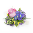 Pinned against a pristine white background, this delicate corsage reads like a small love letter in blooms: a single, partly open rose whose petals graduate from a soft lavender-pink at the heart to a vivid, fuchsia edge, its velvety curves catching cool studio light. To its right, a clustered spray of indigo-purple florets-hydrangea-like in shape-presents tiny bright blue and lime-yellow centers that glint like summer twilight jewels. The flowers are cradled by an assortment of foliage that balances rich colour with tactile contrast: broad variegated ivy leaves with deep emerald centres and luminous golden-yellow margins; slender, silvery-green blades that could be lavender foliage, offering a muted, fragrant suggestion; and a striped green-and-cream leaf artfully curled to add sculptural line. Wisps of fine, asparagus-fern-like greenery breathe airiness between the larger shapes, while a filigree of dark purple mesh peeks from underneath, its web-like texture lending modern depth and a touch of shimmer. At the lower right, a short strand of lustrous white pearls is threaded into the composition, hinting at a wristlet or lapel loop and nodding to tradition. The overall impression is quietly celebratory-romantic but contemporary-meant for weddings, proms, or intimate gatherings. Imagined in the soft morning light of a Highgate preparation table, the piece suggests the comforting scent of rose and the soft, uplifting green notes of fresh foliage, a tiny wearable bouquet crafted with attentive hands for cherished moments in and around Highgate Village and nearby Hampstead.