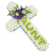 A meticulously arranged floral cross, ideal for a funeral or remembrance service in Highgate, is displayed against a bright white background, allowing its structure and colours to stand out with clarity. The outer edge of the cross is wrapped in a smooth, vivid green ribbon or foliage, giving a crisp, defined outline that emphasises the sacred shape. Inside this border, the cross is densely filled with small white spray chrysanthemums, their numerous, close-fitting blooms creating a thick, soft cushion of petals along both arms and the longer vertical length. The uniform whiteness suggests purity, peace, and a quiet farewell. Running centrally down the vertical arm is a distinctive band of lime-green button chrysanthemums, their domed, rounded heads forming a bright, fresh stripe that contrasts gently with the surrounding white. Over this green strip, fine pale wires or filaments are laid in a delicate criss-cross arrangement, adding an intricate, almost lace-like texture without overwhelming the flowers. At the point where the cross's arms intersect, a carefully composed focal spray of accent blooms adds depth and warmth. Deep purple lisianthus flowers, with their velvety, gently ruffled petals, are nestled among vibrant lime-green button chrysanthemums that repeat the green from the central band. Around this cluster, feathery dark green fern fronds and select foliage fan out slightly, softening the geometric lines and lending the design a touch of natural, woodland character. The balanced tones of white, green, and purple create an atmosphere of reverence and hope, resulting in a floral cross tribute that feels both classic and quietly contemporary for memorial occasions in the Highgate area.