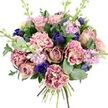 This bouquet, set against a clear white backdrop, feels like an intimate moment of calm captured in flowers. At its heart are generous garden roses in muted blush, dusty mauve, and antique rose, their spiralling petals opening slowly and giving the arrangement a soft, nostalgic centre. Encircling them, layers of frilled carnations create a gentle halo of texture, with petals that move from creamy beige and pale pink at the centre to richer rose and fuchsia at the outer edges, catching the light along every ruffle. Deep indigo and royal blue blossoms wind gracefully through the warmer tones-some as tight, tulip-like buds, others as an open anemone with a dark, velvety centre that adds an almost cinematic depth. Pale lilac and lavender stock stems rise delicately among the larger flowers, their clusters of tiny blooms lending an impression of lightness and a faint, powdery floral scent. The whole design is wrapped in fresh greenery: glossy, dark leaves and silvery-green eucalyptus with rounded forms that offer cool contrast and suggest a clean, aromatic note when the bouquet is lifted. The hand-tied stems at the base reveal its freshly prepared nature, ready to be delivered across Highgate, perhaps to a quiet street near Waterlow Park or a home overlooking Pond Square. The mood is one of understated romance and comfort, making it perfect for an anniversary, a heartfelt thank-you, or simply to bring a touch of softness into a room filled with North London light.