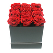 A chic, eye-level photograph features a modern rose box whose clean lines and rich colours echo the sophisticated charm of Highgate. At the heart of the image is a square, matte black container, minimalist in design yet clearly crafted with attention to detail. Its sides are smooth and unadorned except for a fine white band that encircles the lower section, adding a refined, graphic touch reminiscent of contemporary interior design. From the open top of the box rise twelve exquisite red roses, packed closely together in three even rows of four. Each bloom is at the same, fully open stage, with petals arranged in tight, velvety spirals that form full, rounded heads. The roses are a deep crimson red, with nuanced shifts in tone that hint at their lush texture and depth. Their heads sit slightly higher than the rim, creating a sculpted, cushion-like surface of colour that appears almost seamless, as though the top of the box has been paved in petals. The backdrop is a pure, seamless white, which strips away any distraction and allows the dramatic interplay of red and black to dominate the scene. Gentle, diffuse lighting bathes the arrangement, revealing the softness of the petals and the crisp, architectural edges of the box without creating harsh contrasts. The overall impression is one of polished elegance and intense emotion, ideal for delivery to a townhouse just off Highgate High Street, a romantic surprise for a home backing onto Highgate Wood, or a stylish declaration of love placed on a windowsill overlooking the London skyline. It suggests a preserved or long-lasting rose design chosen to keep a special moment alive well beyond the day it is given.