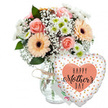 A cheerful Mother's Day gift set is arranged against a clean white background, with the carefully balanced composition drawing attention to every blossom and detail, as if styled in a Highgate florist studio before local delivery. The central element is a clear glass vase, simple and cylindrical, its neck encircled with a small bow of natural twine that adds a rustic, homely charm. Emerging from the vase is a generous mixed bouquet. Several peach-pink roses are caught at their most beautiful point of opening, their soft petals unfurling in gentle spirals that create a sense of depth and luxury. Interspersed among them are large peach gerbera daisies with velvety petals and deep, dark brown centres that offer a striking contrast and a joyful, contemporary feel. Filling the spaces between the larger blooms, tiny white gypsophila flowers float like a fine mist, while compact white chrysanthemums with pale green hearts contribute fullness and structure. Lush green foliage supports and frames the pastels, giving the bouquet a fresh-from-the-garden look that recalls nearby Highgate woodlands and hidden courtyards. Just behind the flowers, a small white greeting card is tucked discreetly, its colourful writing slightly out of focus but clearly intended as a heartfelt Mother's Day note. To the right of the vase, a heart-shaped Mylar balloon rests against the arrangement. The balloon is white and scattered with metallic gold and silver dots that shimmer softly, adding a festive note. At its centre, a peach heart outlines the phrase Happy Mother's Day in elegant black script, making the message of love and appreciation unmistakable. The overall impression is of a thoughtful, ready-to-give Mother's Day gift, perfect for brightening a Highgate home with colour, joy, and gratitude.